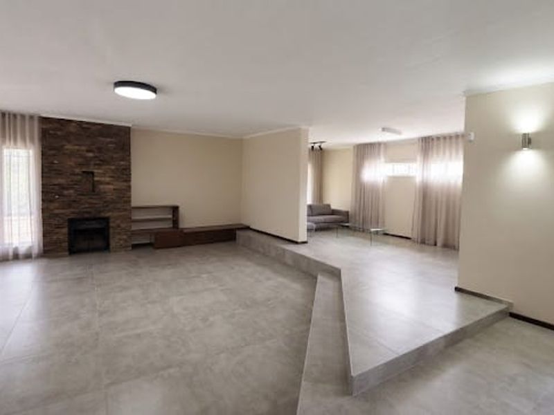Spacious living area featuring a sunken floor design, stone-clad fireplace, and neutral tiled flooring with modern lighting fixtures.