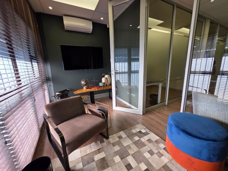 A modern office space featuring laminate flooring, glass partition walls, and a wall-mounted air conditioning unit, providing a professional and well-lit work environment.