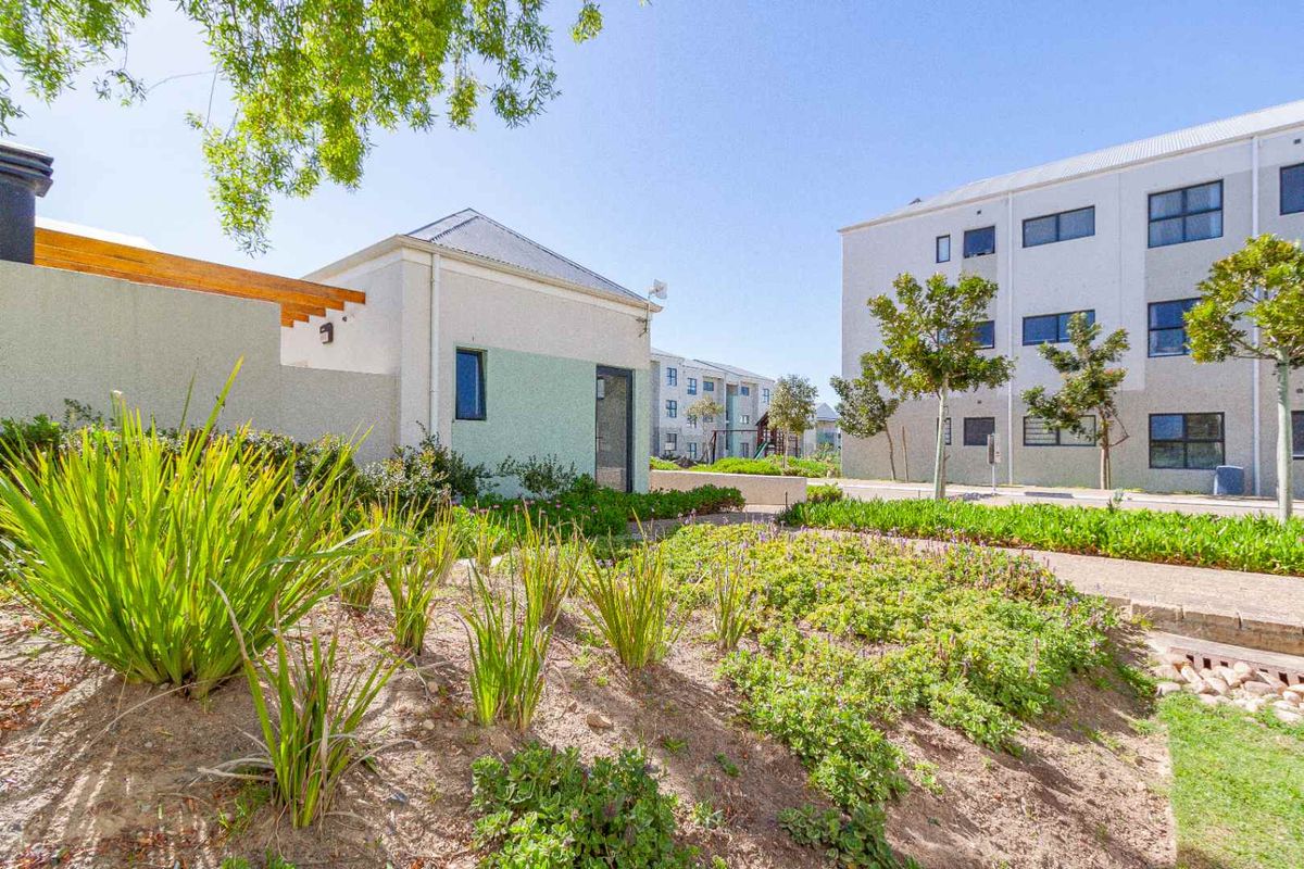 A well-maintained communal garden area featuring landscaped beds, a paved walkway, and a timber pergola set against modern apartment buildings.