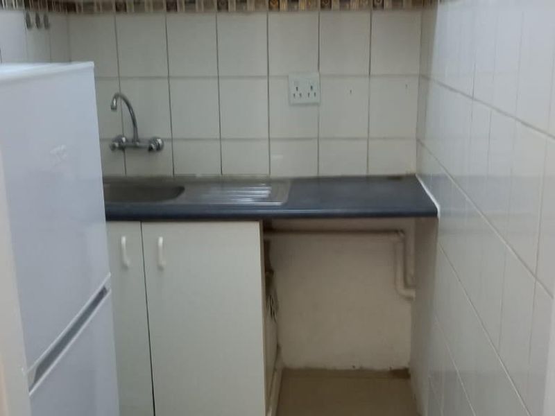 A compact kitchenette featuring a stainless steel sink, tiled backsplash, and basic base cabinetry with laminate countertop.