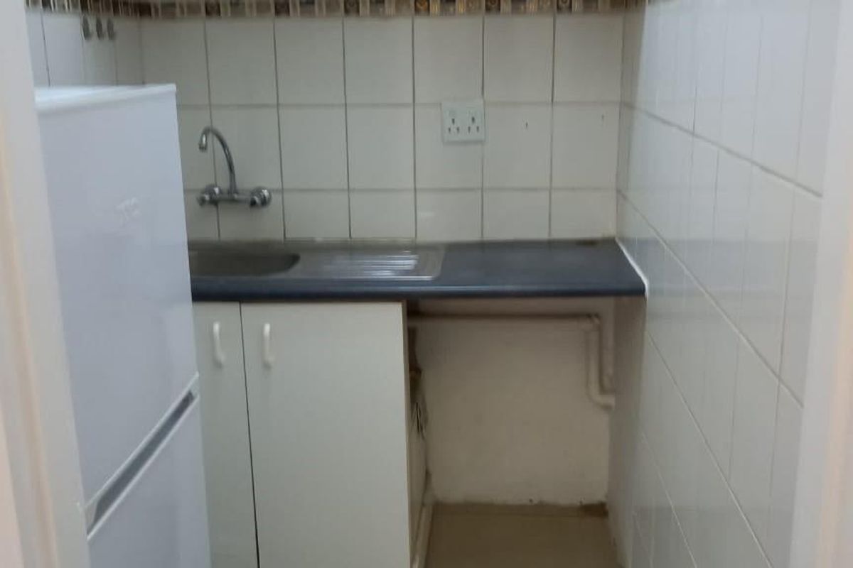 A compact kitchenette featuring a stainless steel sink, tiled backsplash, and basic base cabinetry with laminate countertop.