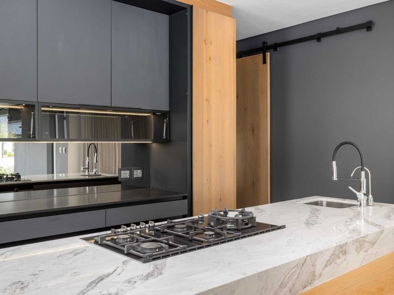 Modern kitchen featuring dark cabinetry, a marble-look stone island with a gas hob, integrated sink, and a sliding timber barn door.