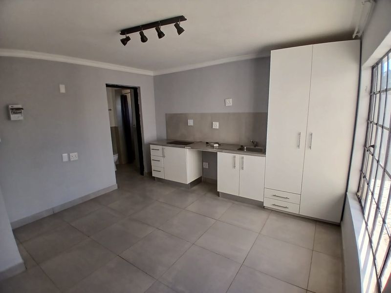 An open-plan living and kitchen area featuring tiled floors, built-in cabinetry, a sink, a hob, and security bars on the windows.