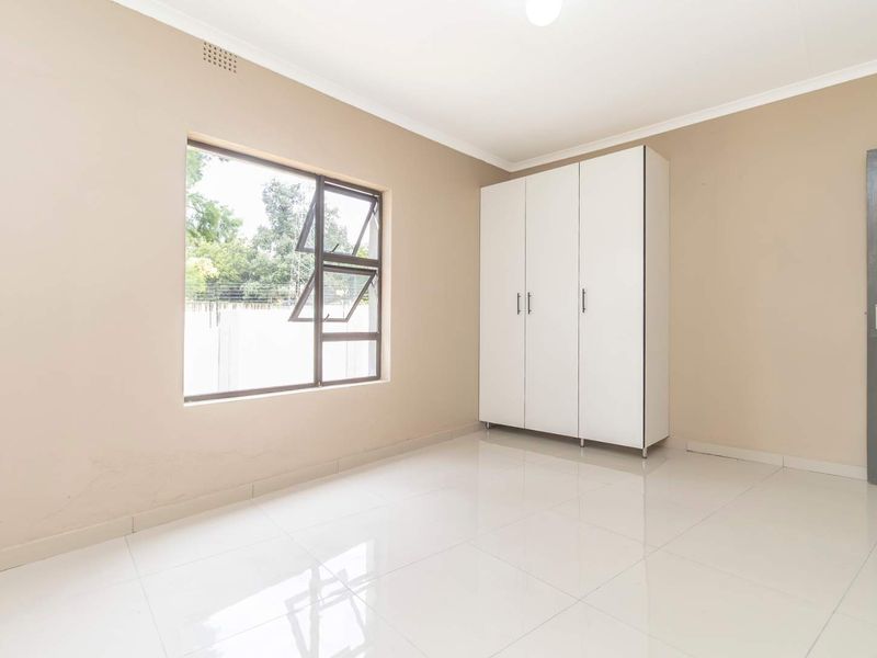 A bright, empty bedroom featuring neutral wall tones, white tiled flooring, and a built-in white wardrobe.