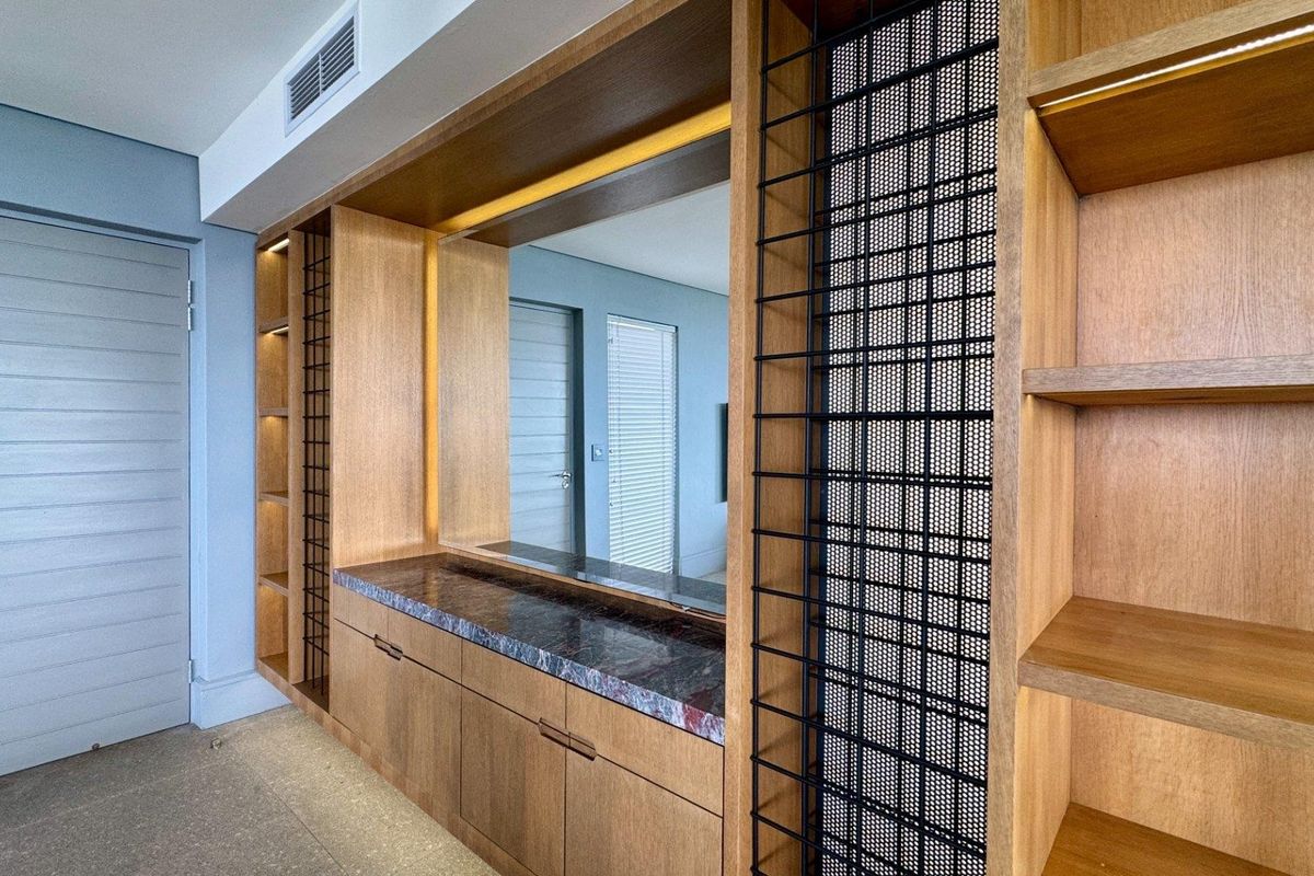 Modern living area featuring custom built-in wooden cabinetry with integrated lighting, stone countertop, and decorative metal mesh shelving.