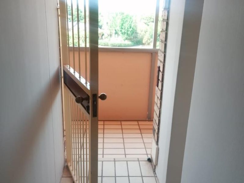 A view through a security gate onto a tiled balcony area with a brick archway feature.
