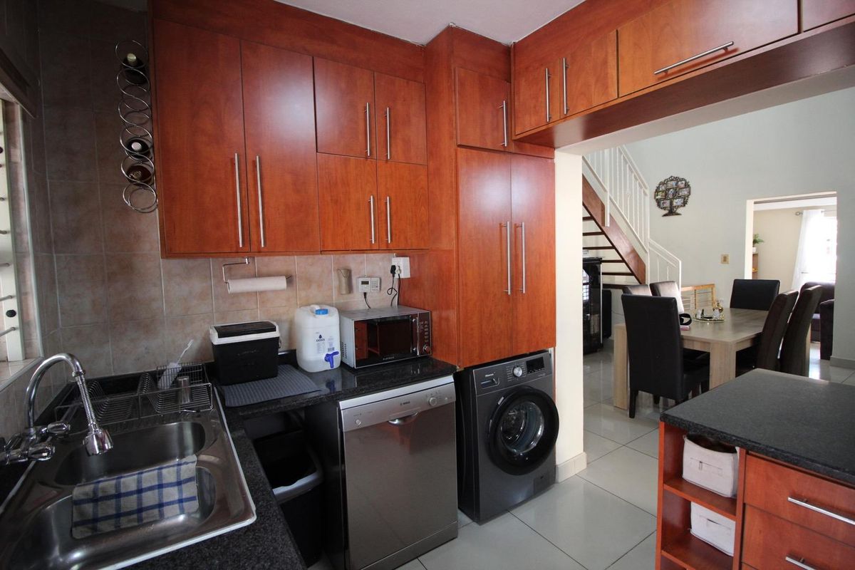 A functional kitchen featuring wood-finish cabinetry, granite countertops, a double sink, and integrated space for a dishwasher and washing machine.