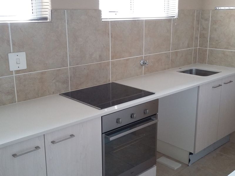 A functional kitchen area featuring a built-in oven, electric hob, stainless steel sink, and tiled backsplash with light-toned cabinetry.