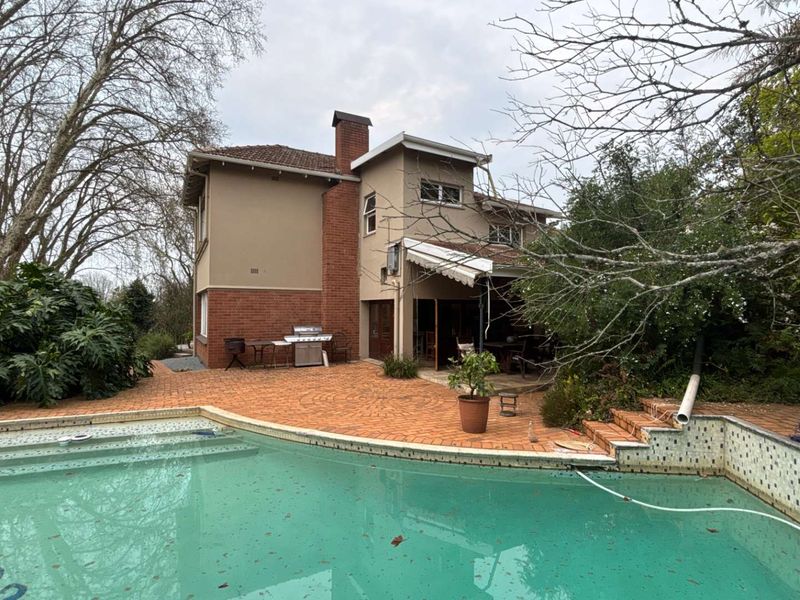Rear exterior view featuring a swimming pool, brick paved patio area, and a multi-story residence with a prominent brick chimney.