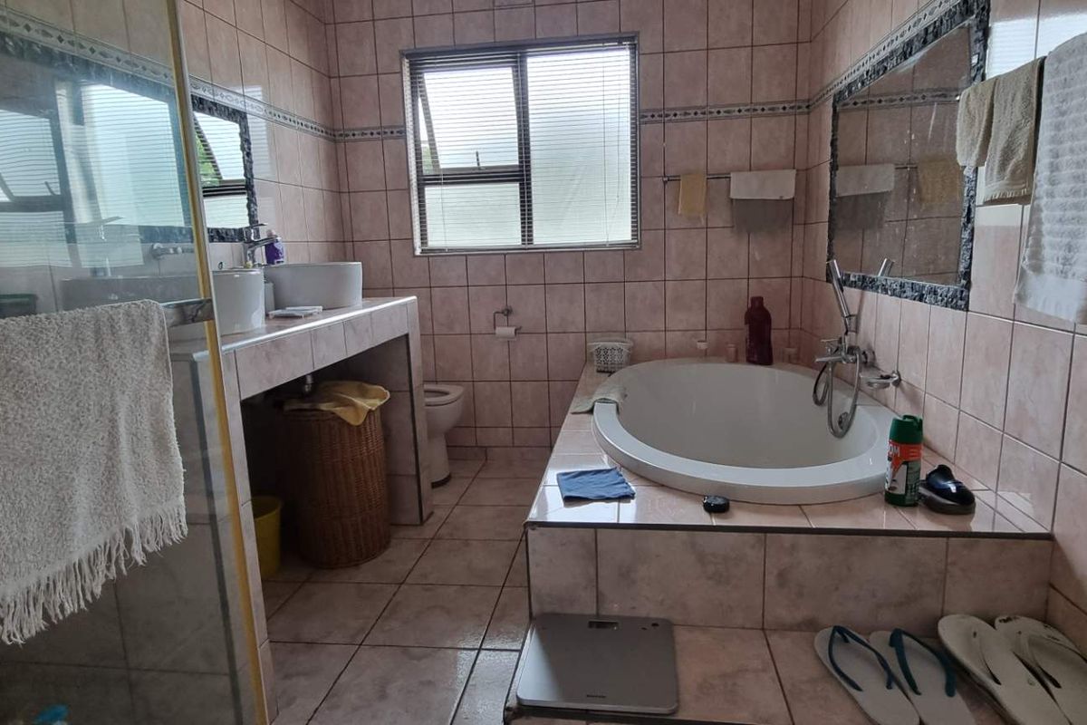 A functional bathroom featuring a built-in bathtub, a separate glass-enclosed shower, and a vanity basin with tiled finishes.