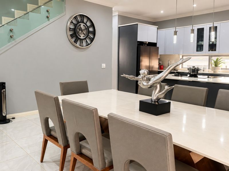 Modern open-plan living area featuring a sleek kitchen with stone countertops, glass staircase balustrade, and polished tiled flooring throughout.