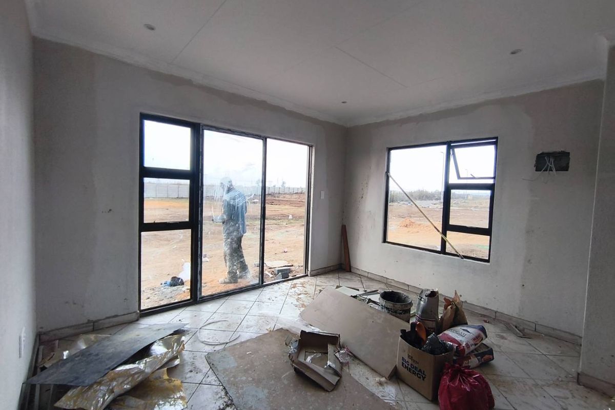 An unfinished living area featuring tiled flooring, large aluminium-framed windows, and sliding doors, currently undergoing construction and interior finishing.