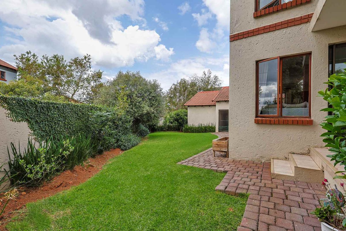 A well-maintained rear garden featuring a paved patio area, lush lawn, and established perimeter hedging, providing a private outdoor space.
