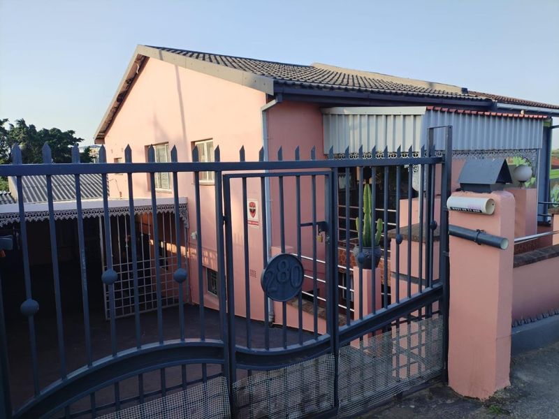 Front exterior view of a residential property featuring a metal security gate, perimeter wall, and covered carport area.