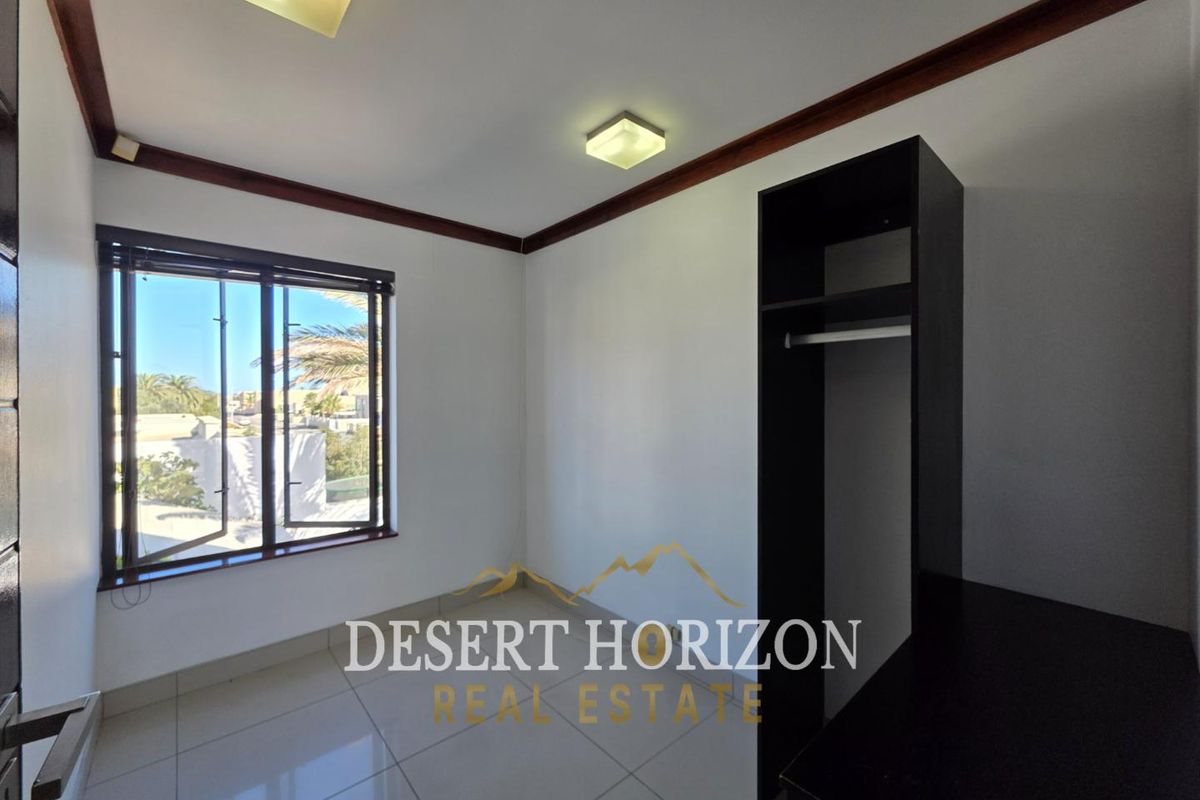 A bright bedroom featuring tiled flooring, built-in storage cabinetry, and a window with exterior views.