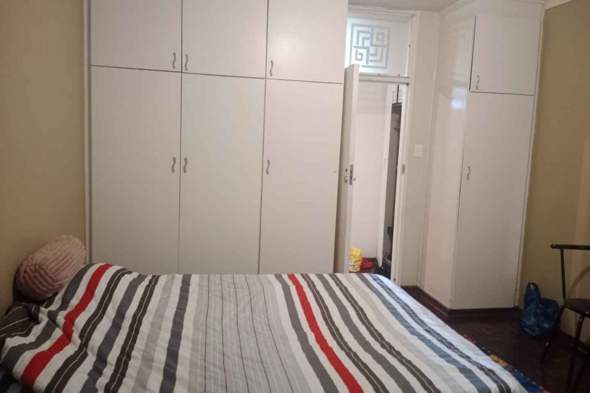 Bedroom featuring extensive built-in floor-to-ceiling cupboards and traditional parquet flooring, offering ample storage space within the apartment.