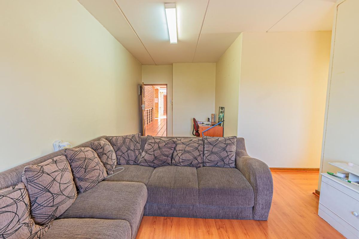 A living room area featuring laminate wood flooring and a central ceiling light fixture, providing a functional space with access to the hallway.