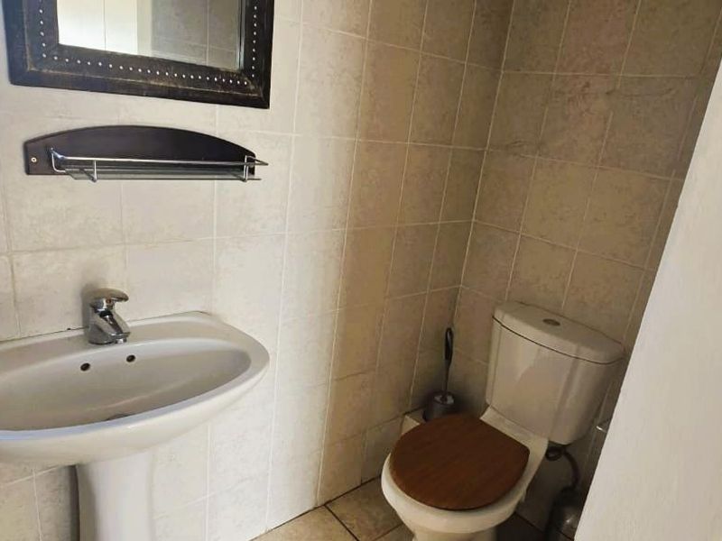 A functional bathroom featuring a pedestal washbasin, toilet, and neutral ceramic wall and floor tiling.