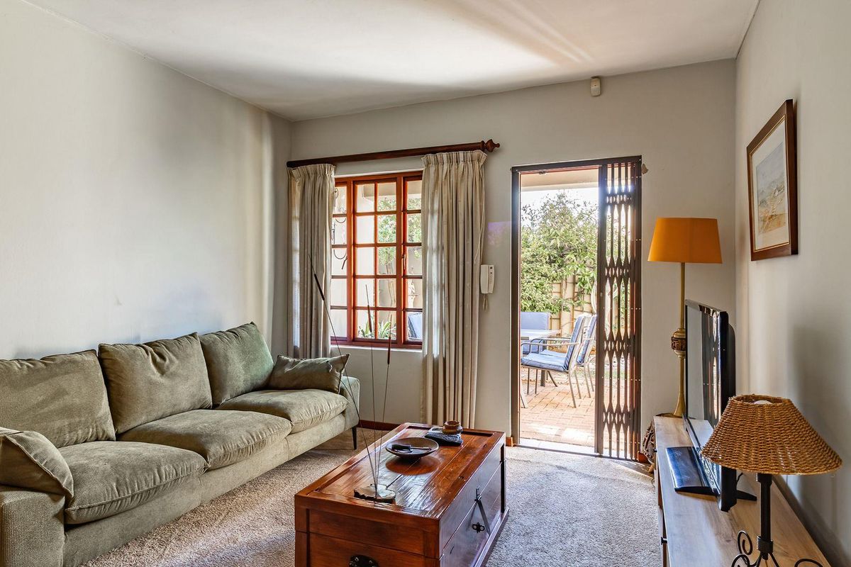 A comfortable living room featuring carpeted flooring, a timber-framed window, and direct access to an outdoor patio area through a security gate.