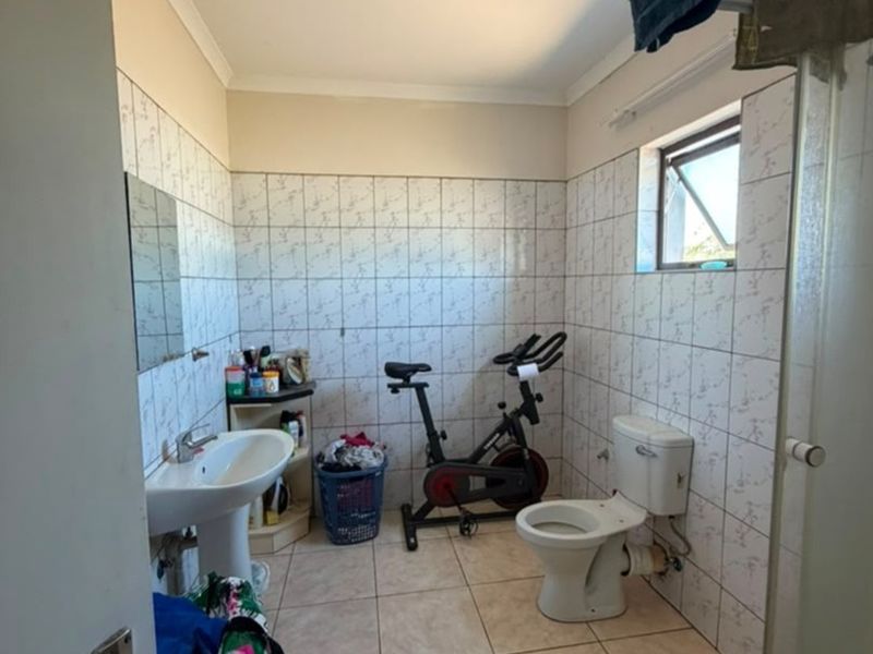A functional bathroom featuring a pedestal basin, toilet, and shower enclosure with tiled finishes, currently used as a multi-purpose space.