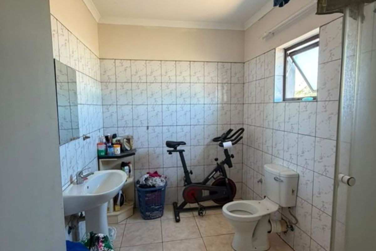 A functional bathroom featuring a pedestal basin, toilet, and shower enclosure with tiled finishes, currently used as a multi-purpose space.