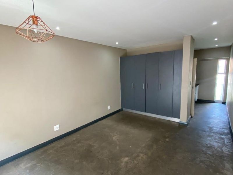 A spacious, empty bedroom featuring modern built-in cupboards, polished concrete flooring, and recessed downlighting, offering a clean and neutral canvas.