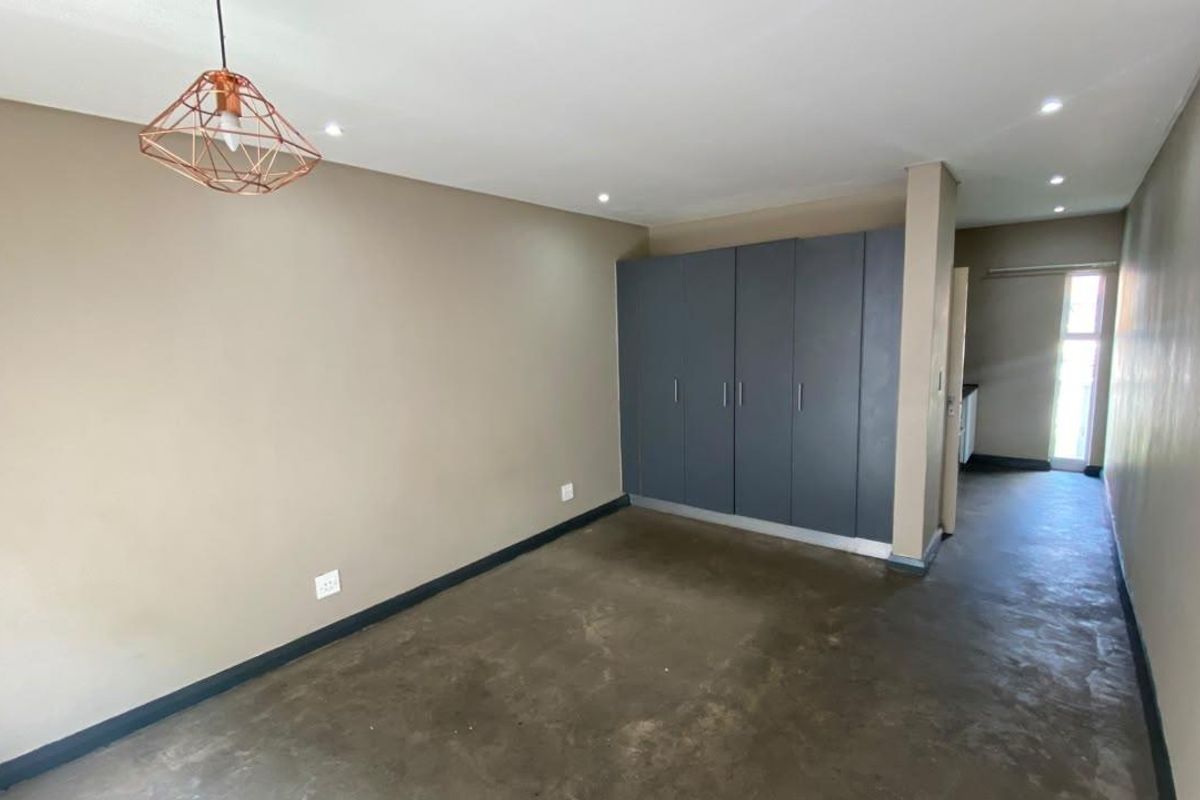 A spacious, empty bedroom featuring modern built-in cupboards, polished concrete flooring, and recessed downlighting, offering a clean and neutral canvas.