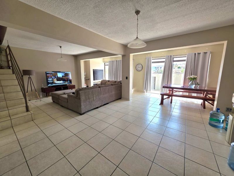Spacious open-plan living and dining area featuring tiled flooring, a staircase, and sliding glass doors leading to an outdoor space.