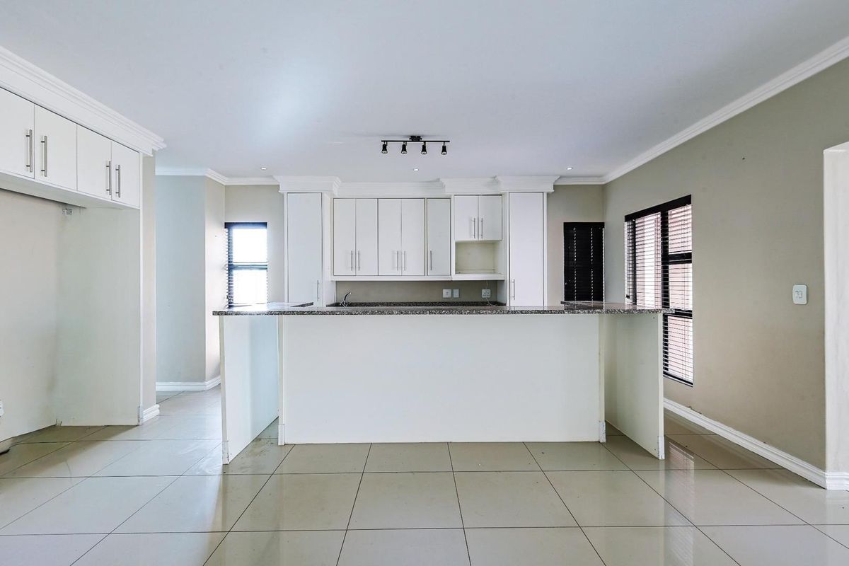 A bright, open-plan kitchen featuring white cabinetry, granite countertops, a central breakfast island, and tiled flooring throughout.