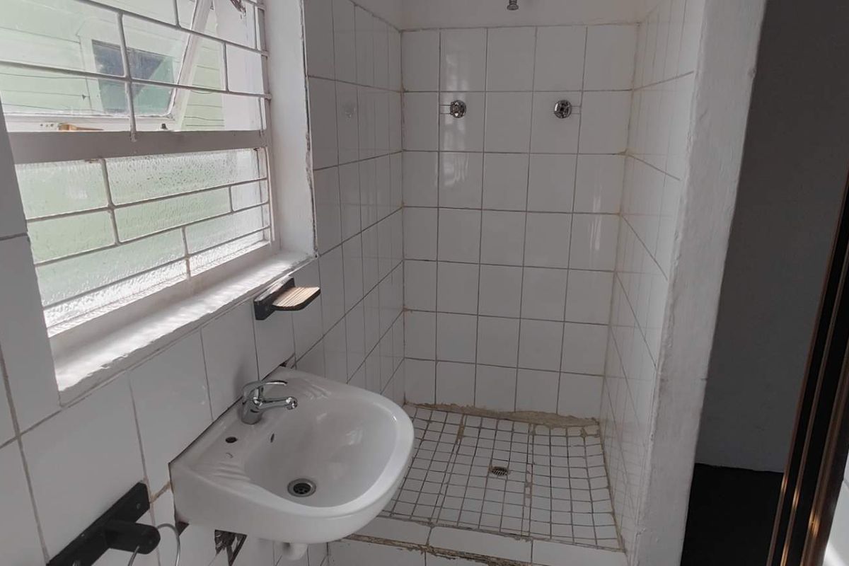 A compact bathroom featuring a wall-mounted basin and a tiled shower enclosure, requiring some maintenance and cosmetic updates to improve its overall condition.