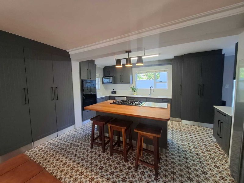 Modern kitchen featuring dark cabinetry, a central island with a wooden countertop, gas cooktop, and decorative patterned floor tiles.