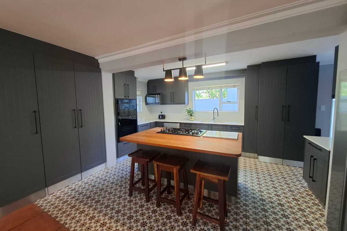 Modern kitchen featuring dark cabinetry, a central island with a wooden countertop, gas cooktop, and decorative patterned floor tiles.