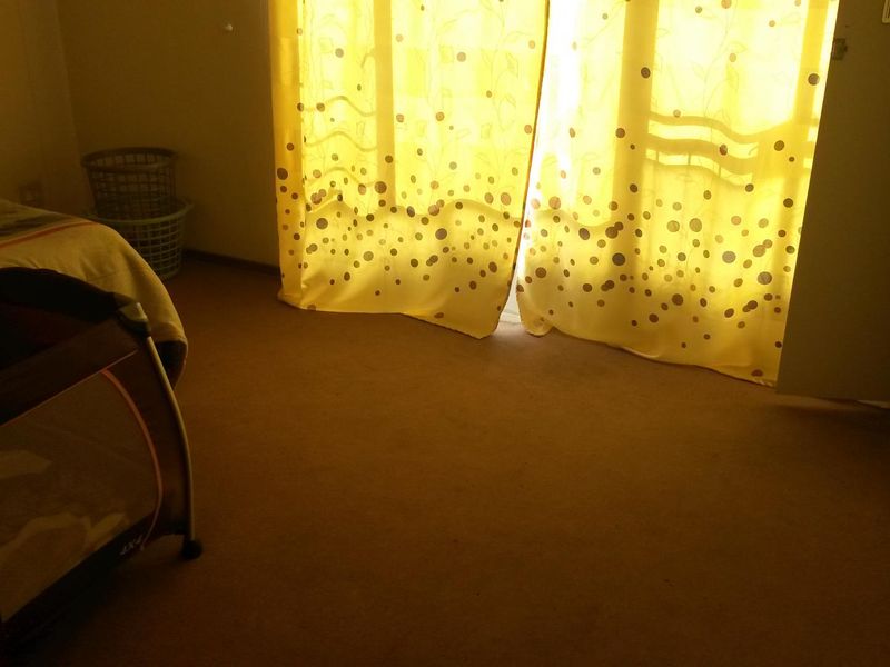A bedroom featuring carpet flooring and natural light entering through a window covered by curtains.