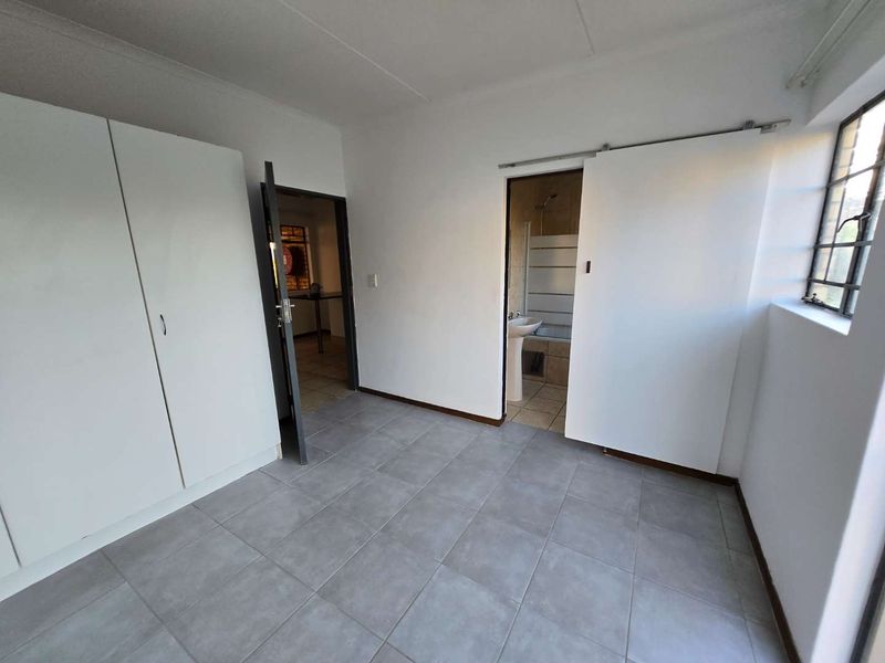 A clean, empty bedroom featuring neutral tiled flooring, built-in cupboards, and an en-suite bathroom access via a sliding door.