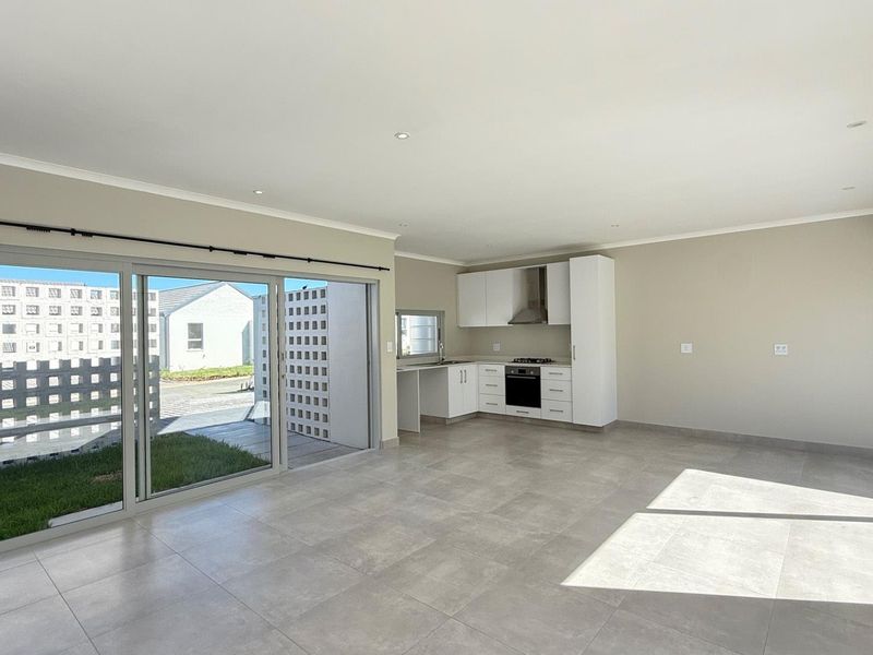 Spacious open-plan living area featuring a modern kitchen with built-in appliances, tiled floors, and large sliding doors leading to an outdoor space.