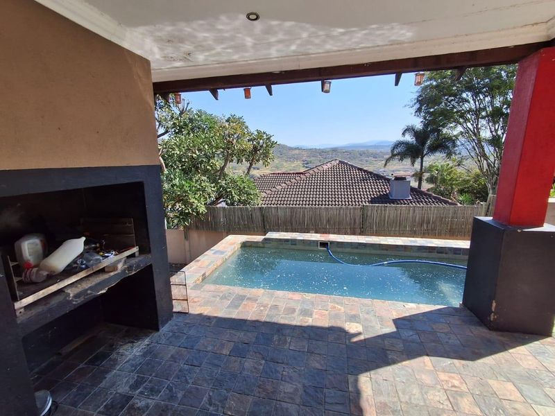 Covered patio area featuring a built-in braai, slate-style tiled flooring, and direct access to a swimming pool with scenic landscape views.