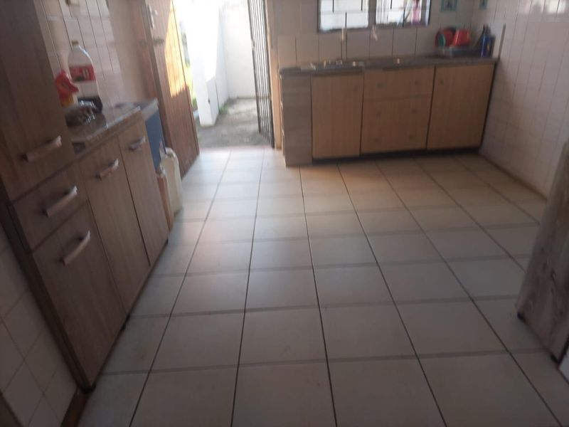 A functional kitchen featuring tiled flooring, wall-to-wall tiling, and built-in wooden cabinetry with direct access to an outdoor area.