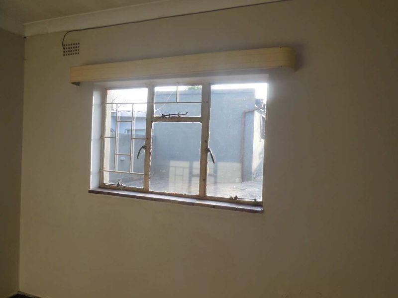 An empty bedroom featuring a steel-framed window with security bars, a wooden curtain pelmet, and coved ceiling cornices, requiring cosmetic updates.