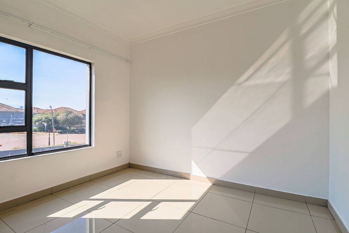 A bright, empty bedroom featuring neutral tiled flooring, clean white walls, and a large window providing natural light.