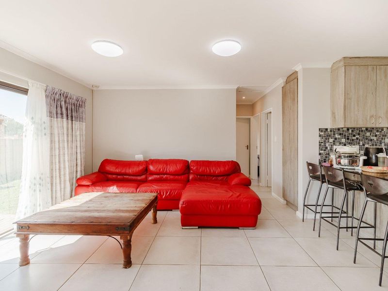 Open-plan living area featuring tiled flooring, a modern kitchen corner with mosaic backsplash, and large sliding doors providing access to the exterior.
