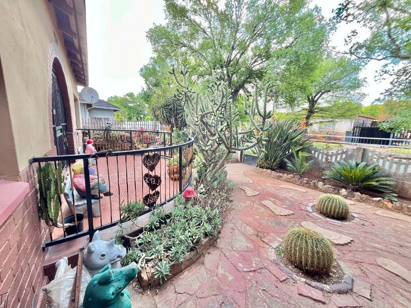 A covered patio area featuring wrought iron railings and paved flooring, leading out to a landscaped garden with stone pathways and established plantings.