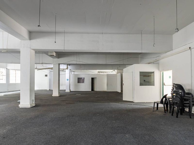 A large, open-plan commercial space featuring industrial concrete columns, exposed beams, and partitioned office areas, suitable for flexible business or retail use.