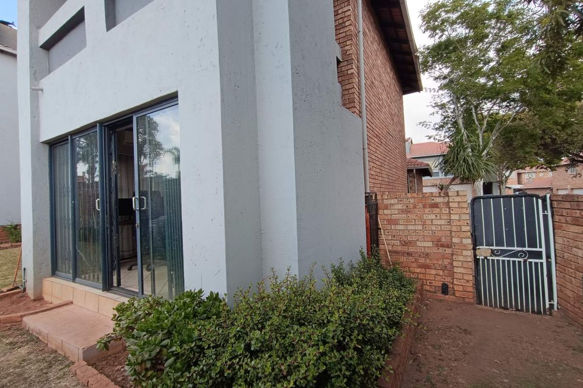 Rear view of the townhouse featuring a brick facade, sliding glass doors, and a private garden area with a gated side entrance.