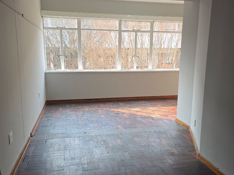 An empty living area featuring original parquet flooring and large windows that provide ample natural light.