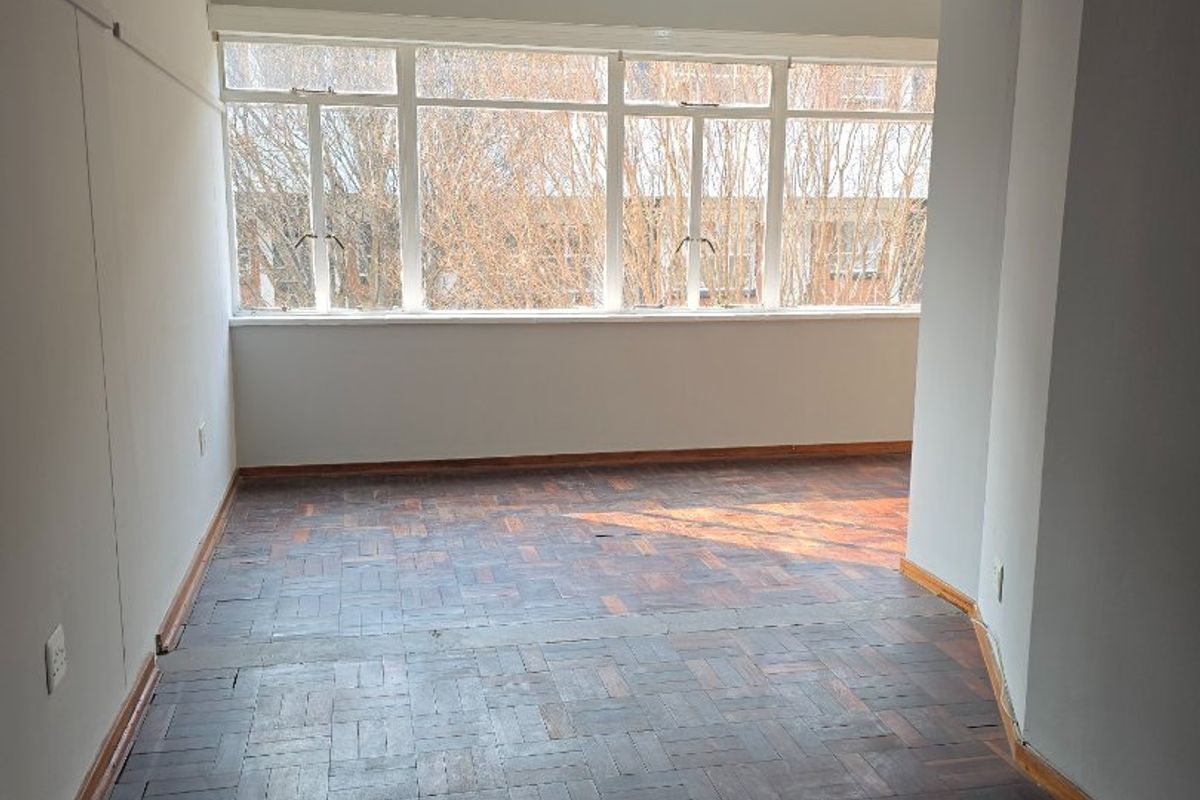 An empty living area featuring original parquet flooring and large windows that provide ample natural light.