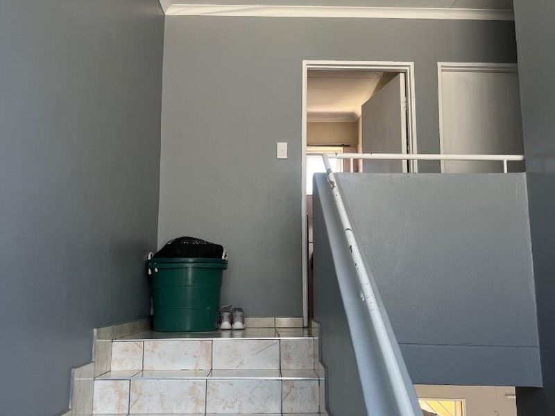 A tiled staircase landing area featuring a metal handrail and neutral grey wall finishes, providing access to upper level rooms.
