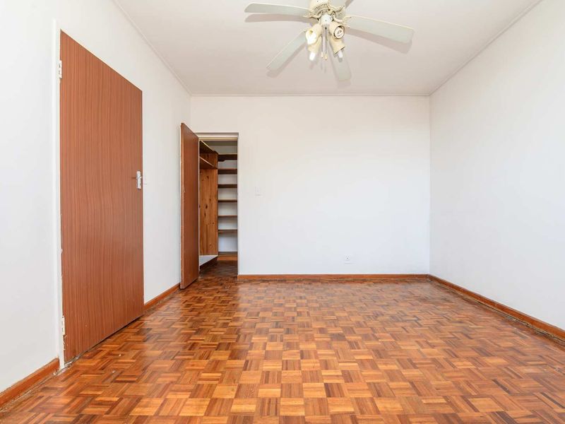 An empty bedroom featuring classic parquet flooring, a ceiling fan, and a built-in closet with shelving.