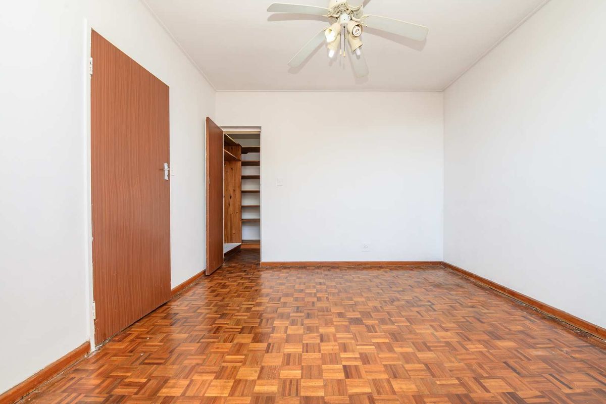 An empty bedroom featuring classic parquet flooring, a ceiling fan, and a built-in closet with shelving.