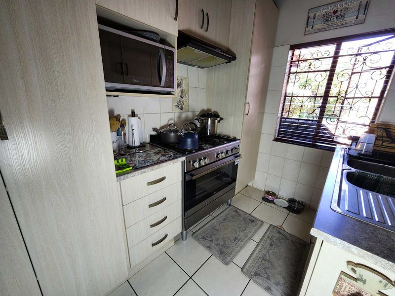 Compact kitchen featuring built-in cabinetry, a gas stove with extractor fan, built-in microwave, and a double sink with tiled finishes.