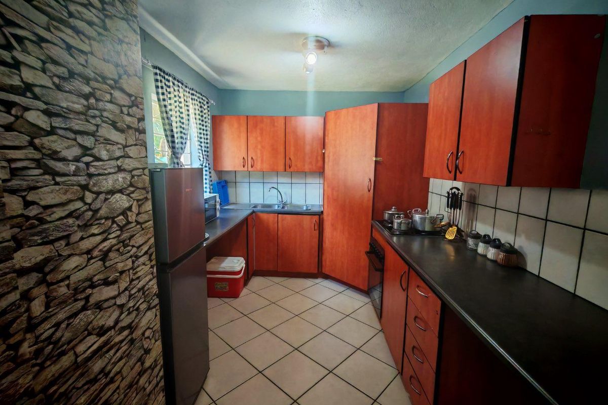 A functional kitchen featuring wood-tone cabinetry, dark countertops, tiled splashbacks, and ceramic floor tiles, offering a practical layout for daily meal preparation.